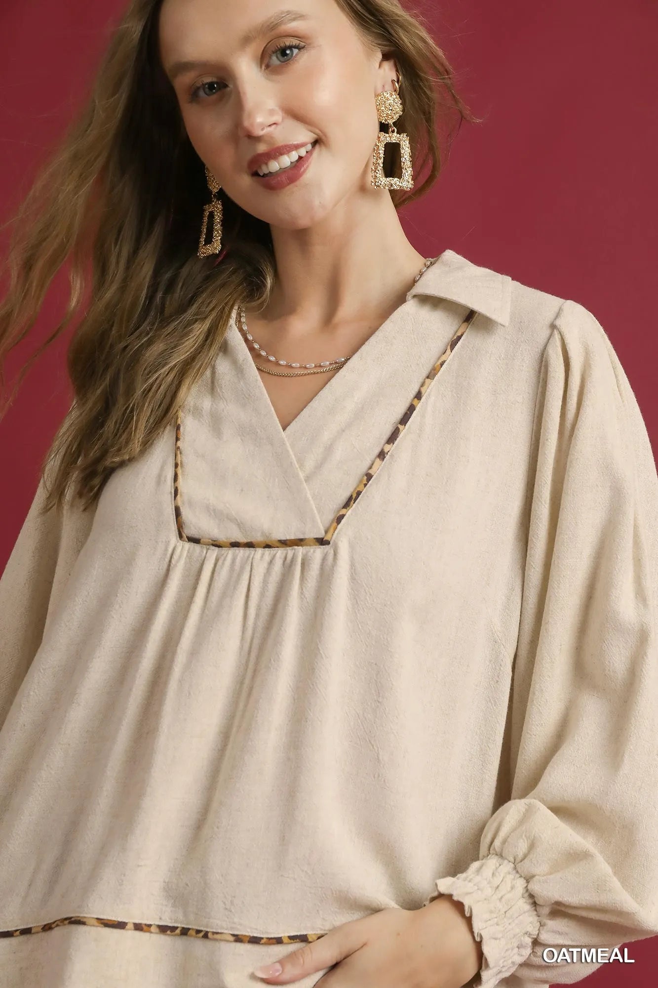 Woman modeling a beige linen scallop hem blouse with contrast trim and V-neck.
