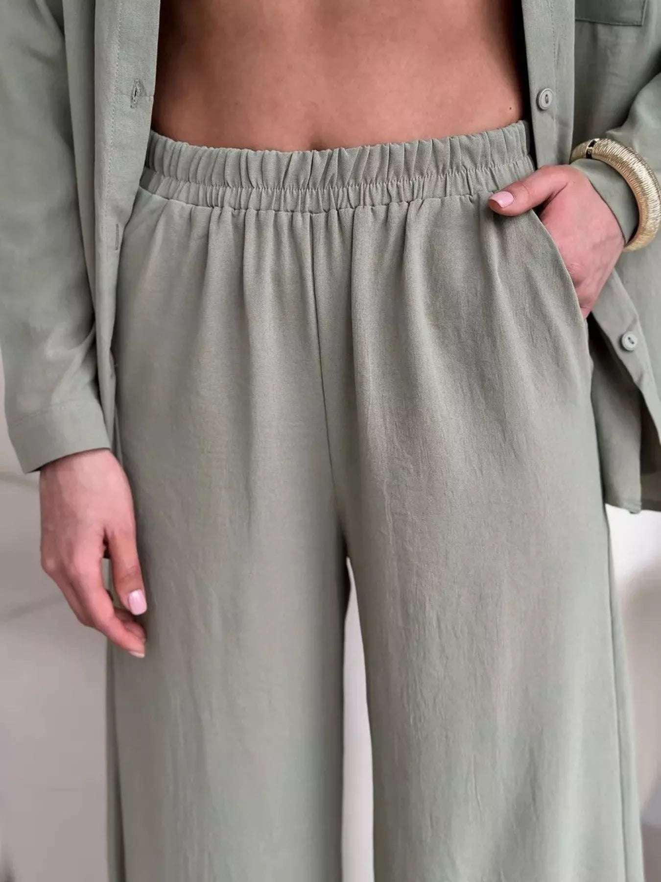 Green two-piece set with open button-down shirt and elastic-waist pants, model posing with hands in pockets.