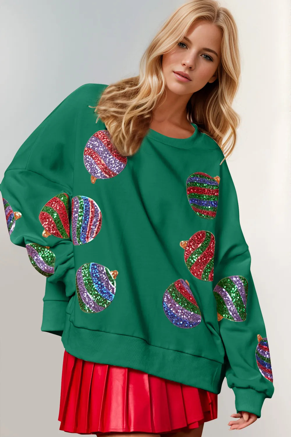 Green long-sleeve sweatshirt with colorful sequin Christmas ornament designs, modeled by a blonde woman.