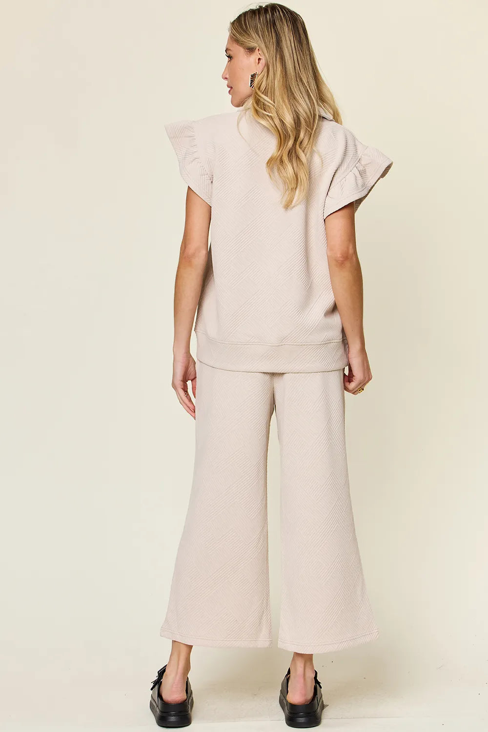 Rear view of a woman in a textured ruffle short sleeve top and wide leg pants set in beige.