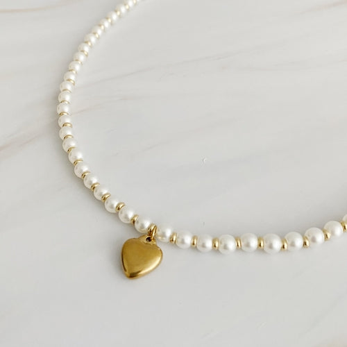 A pearl necklace with alternating gold beads and a gold heart bauble pendant.