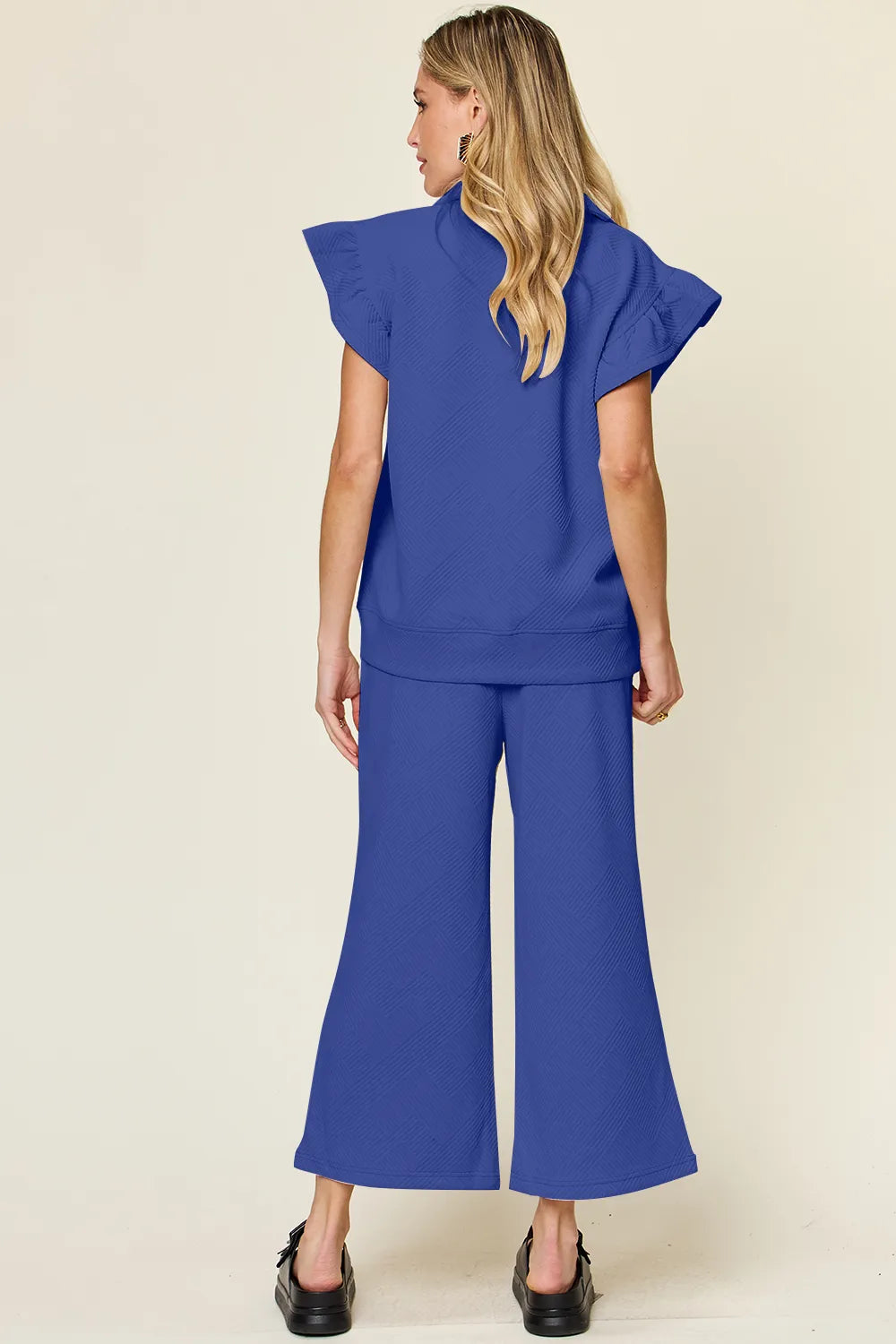 Rear view of a woman in a textured ruffle short sleeve top and wide leg pants set in blue.