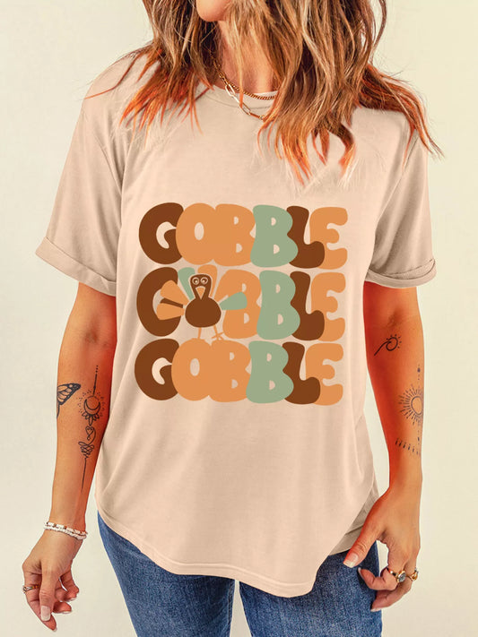 Woman wearing a beige round neck T-shirt with multicolored "Gobble" text and turkey graphic.