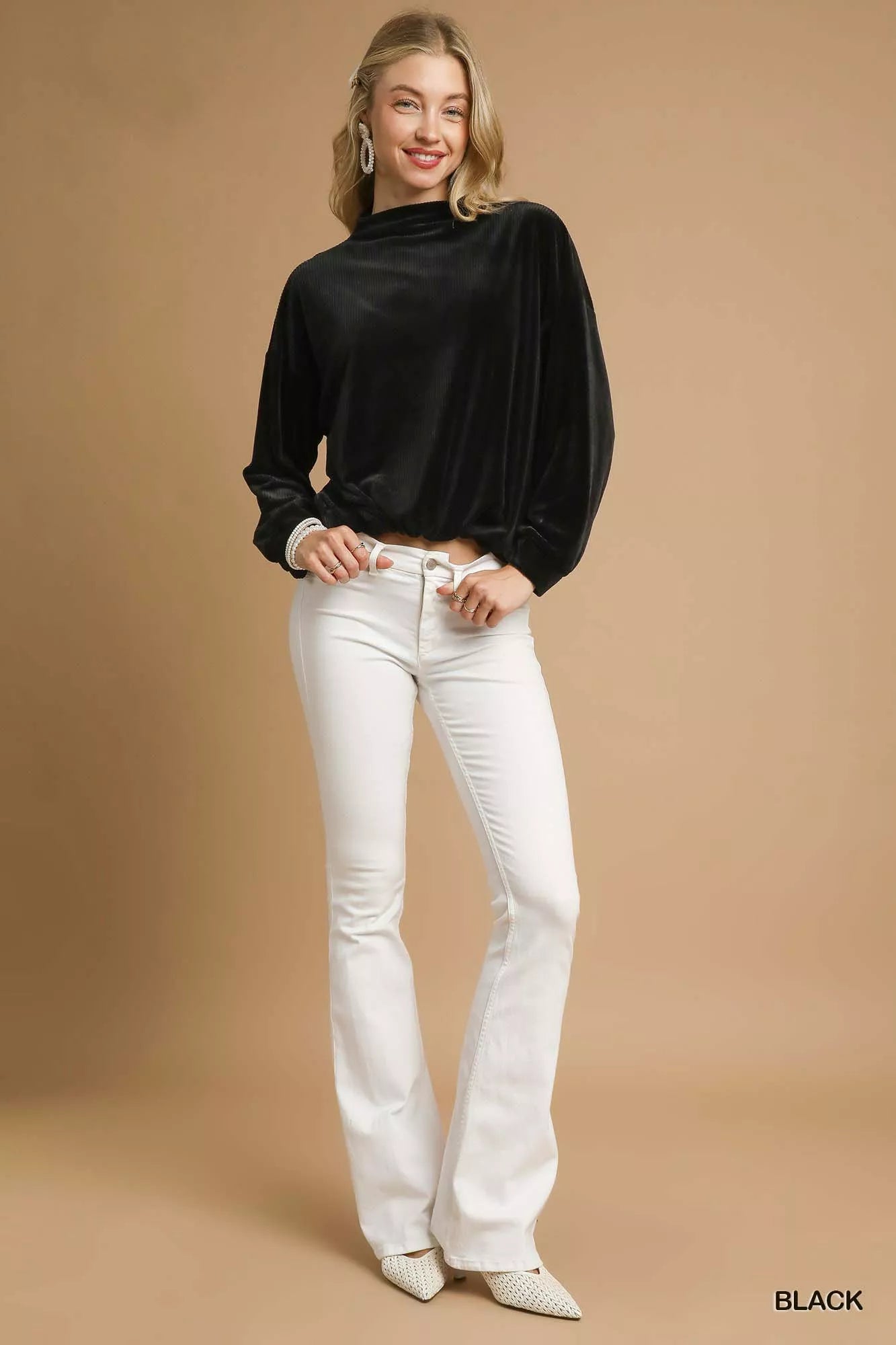Oversized ribbed knit top with drawstring hem in black, modeled with white flared jeans.