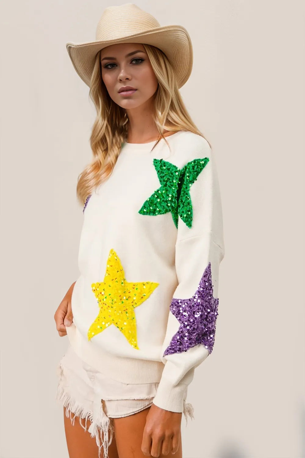 White dropped shoulder sweater with green, yellow, and purple sequin star appliques.