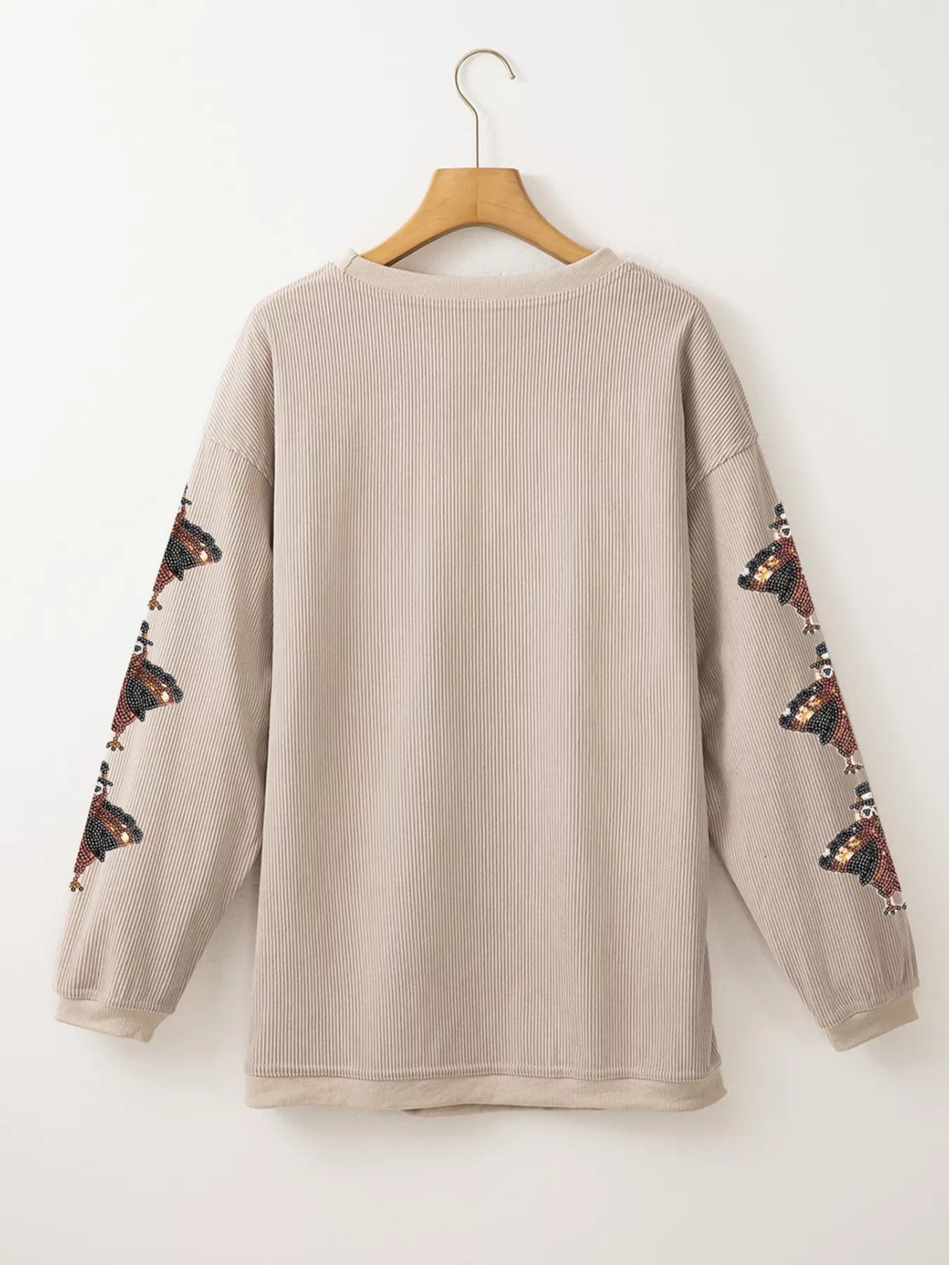 Rear view of gray ribbed sweatshirt with turkey sequin embroidery on sleeves, hanging on a wooden hanger.