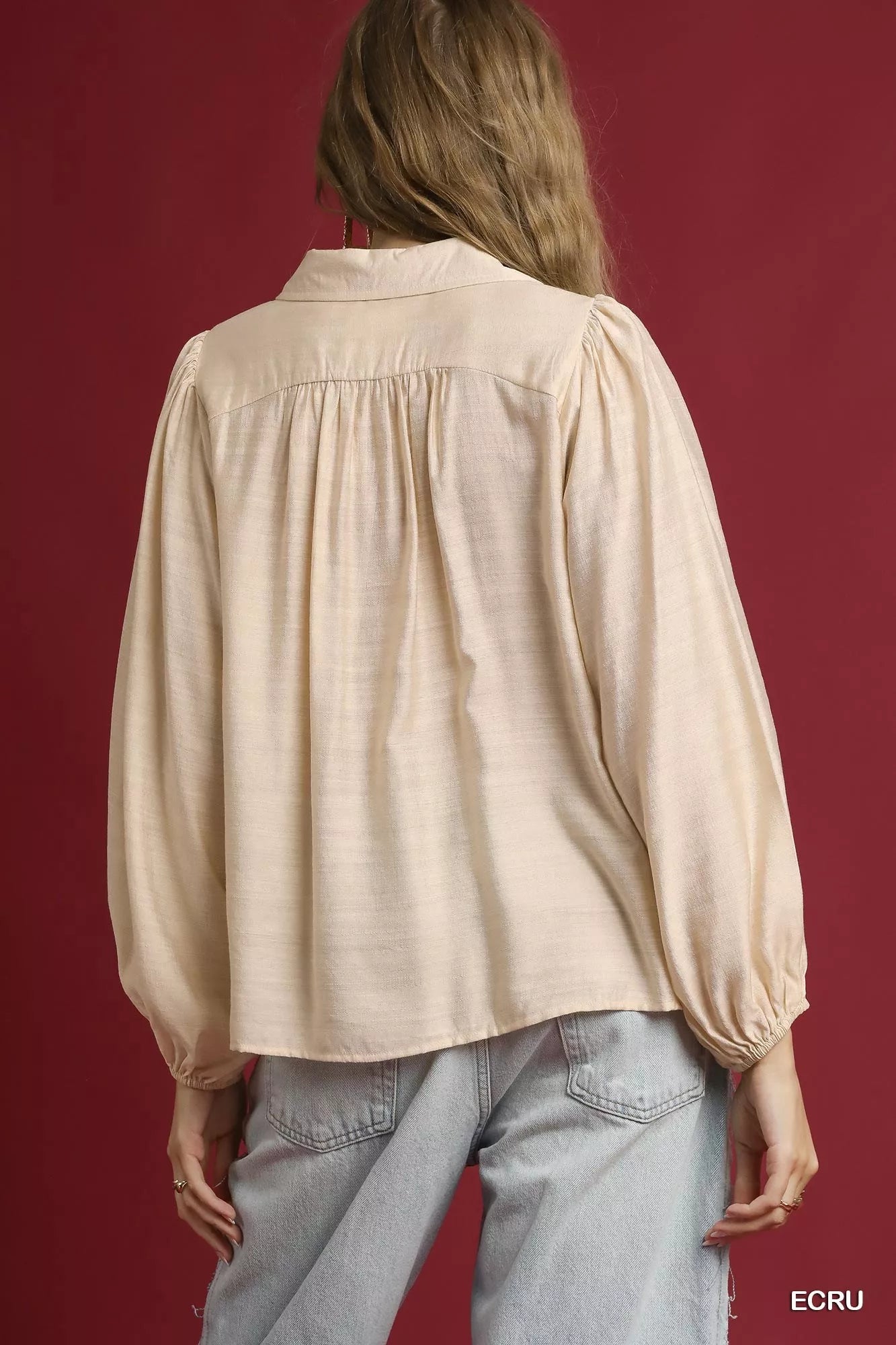 Rear view of a beige long-sleeve blouse with collared neckline and puffed sleeves on a model.