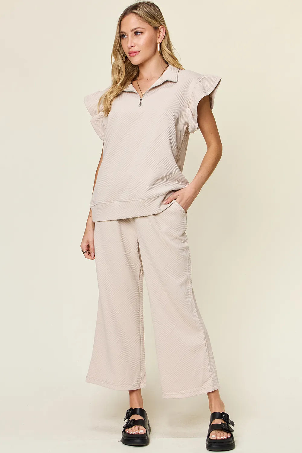 Woman modeling a textured ruffle short sleeve top and wide leg pants set in beige.