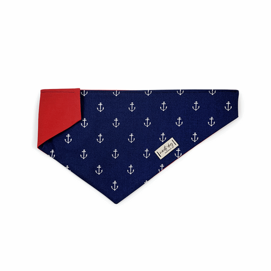Navy blue dog bandana with white anchors and red inner lining designed to fit over collars.