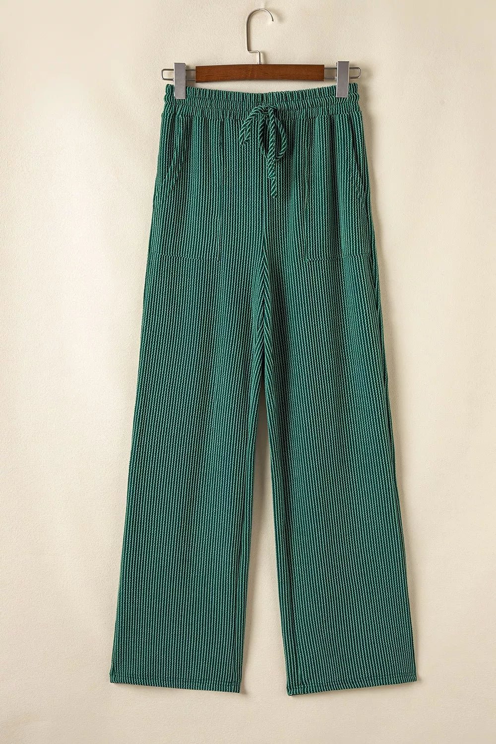 Green polyester drawstring pants with side pockets, hung on a wooden hanger.