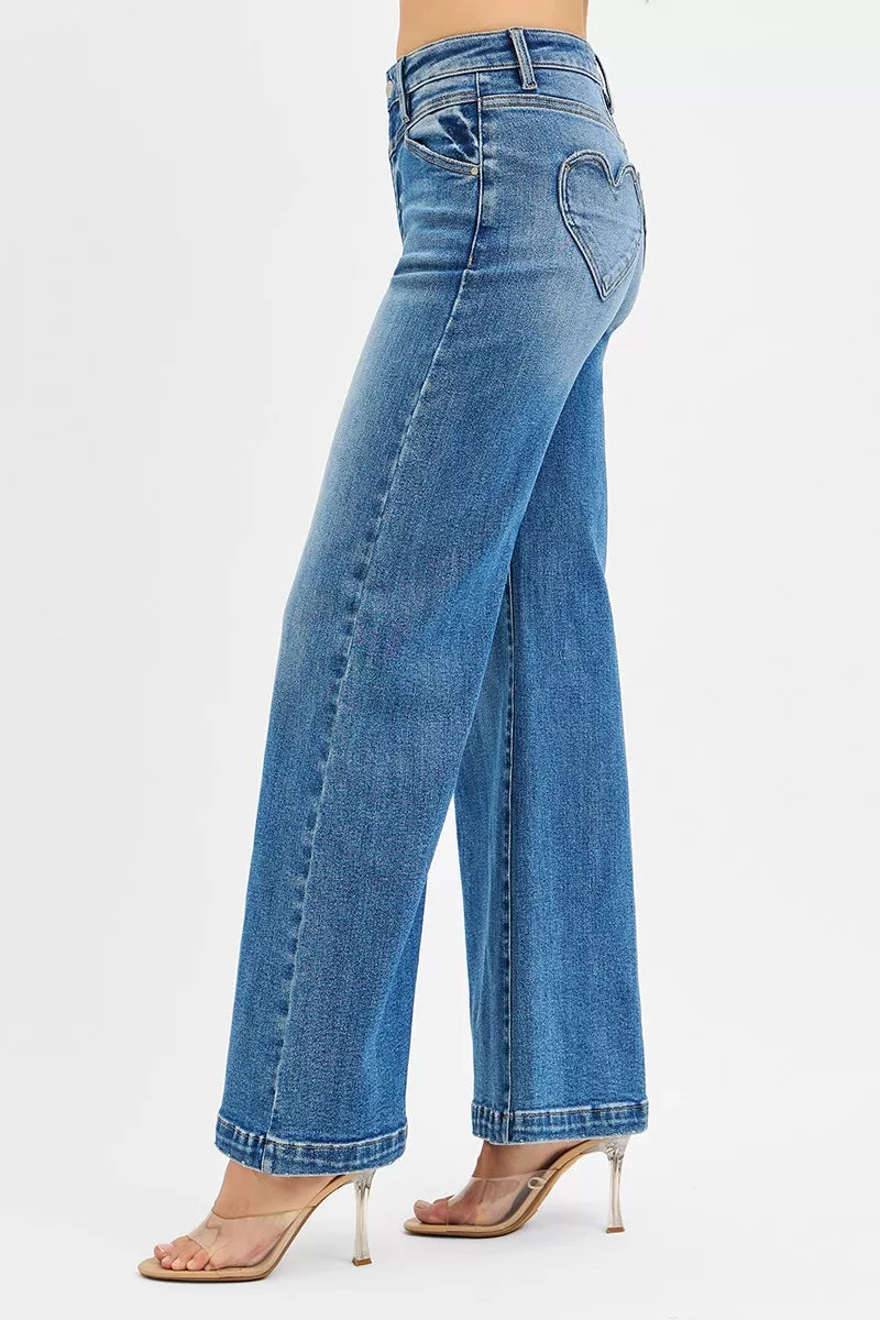 High-rise wide-leg jeans in blue denim with heart-shaped back pockets, modeled from the side.