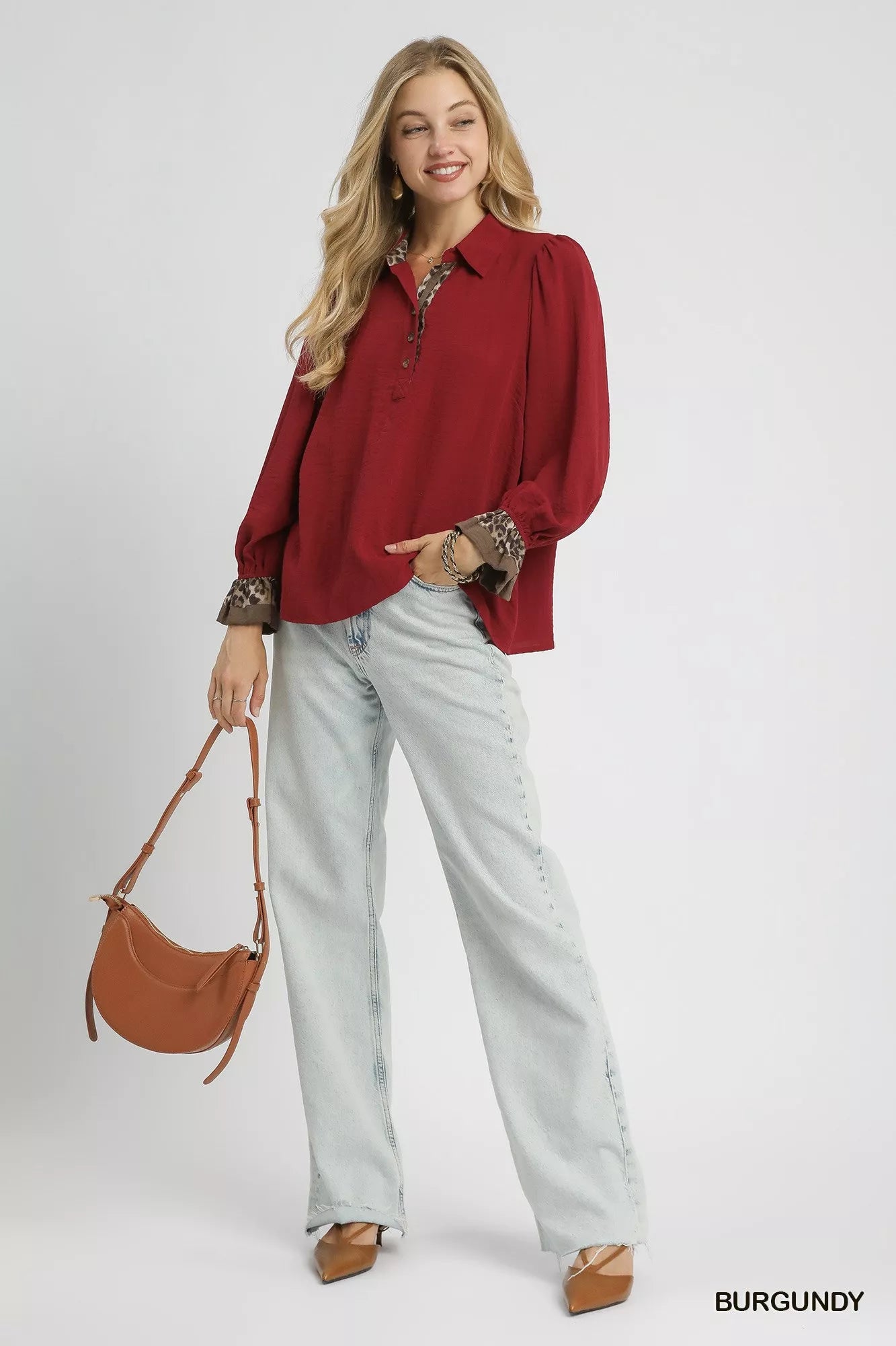 Woman wearing a burgundy half-button blouse with leopard print trim cuffs, paired with light wash jeans and a brown crossbody bag.