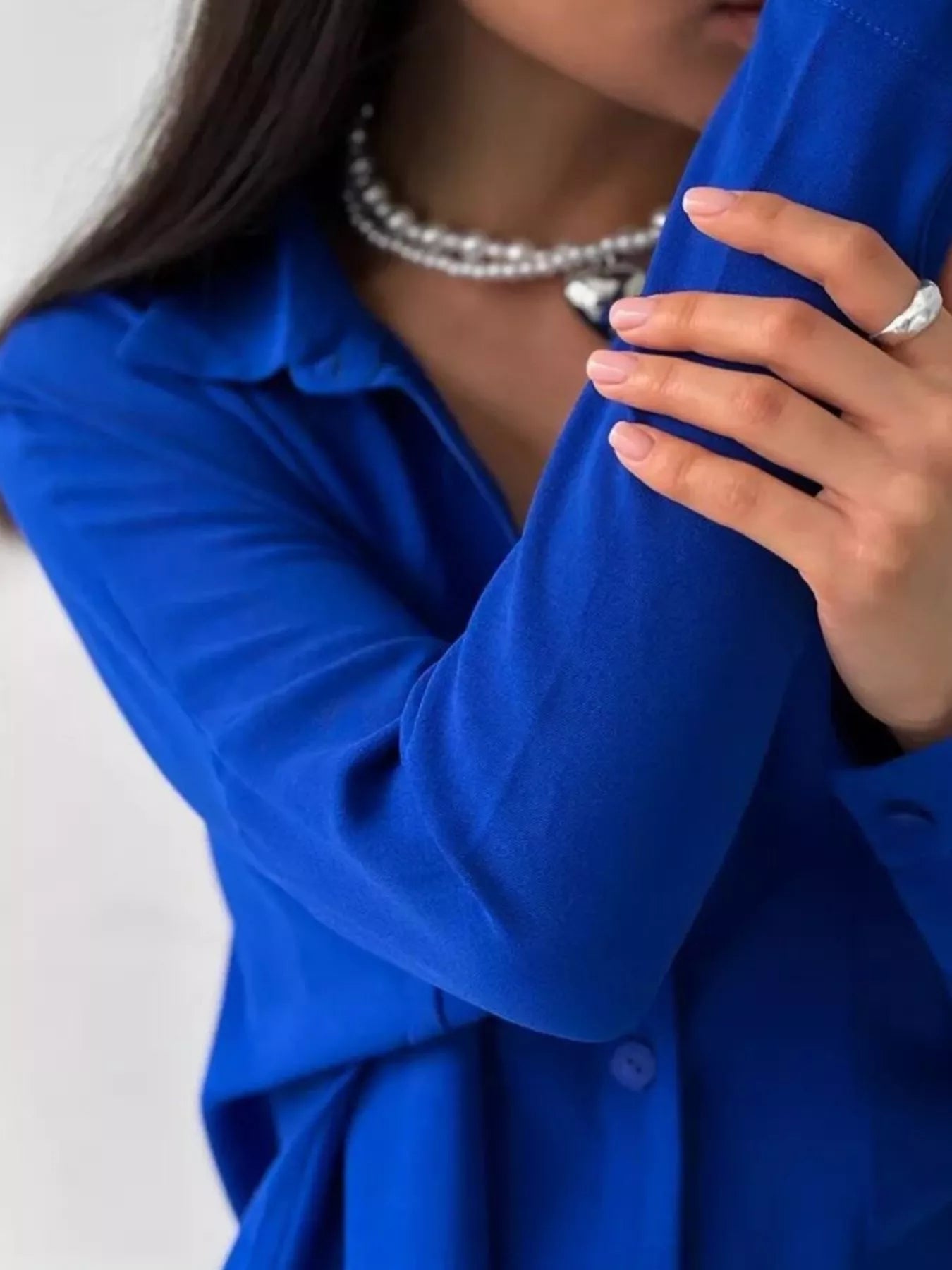 Woman modeling a blue two-piece button-down shirt and pants set with pearl necklace.