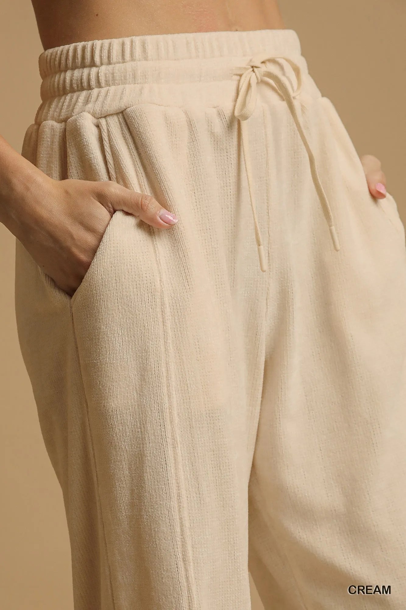Cream drawstring wide-leg pants with flowy fit and side pockets.