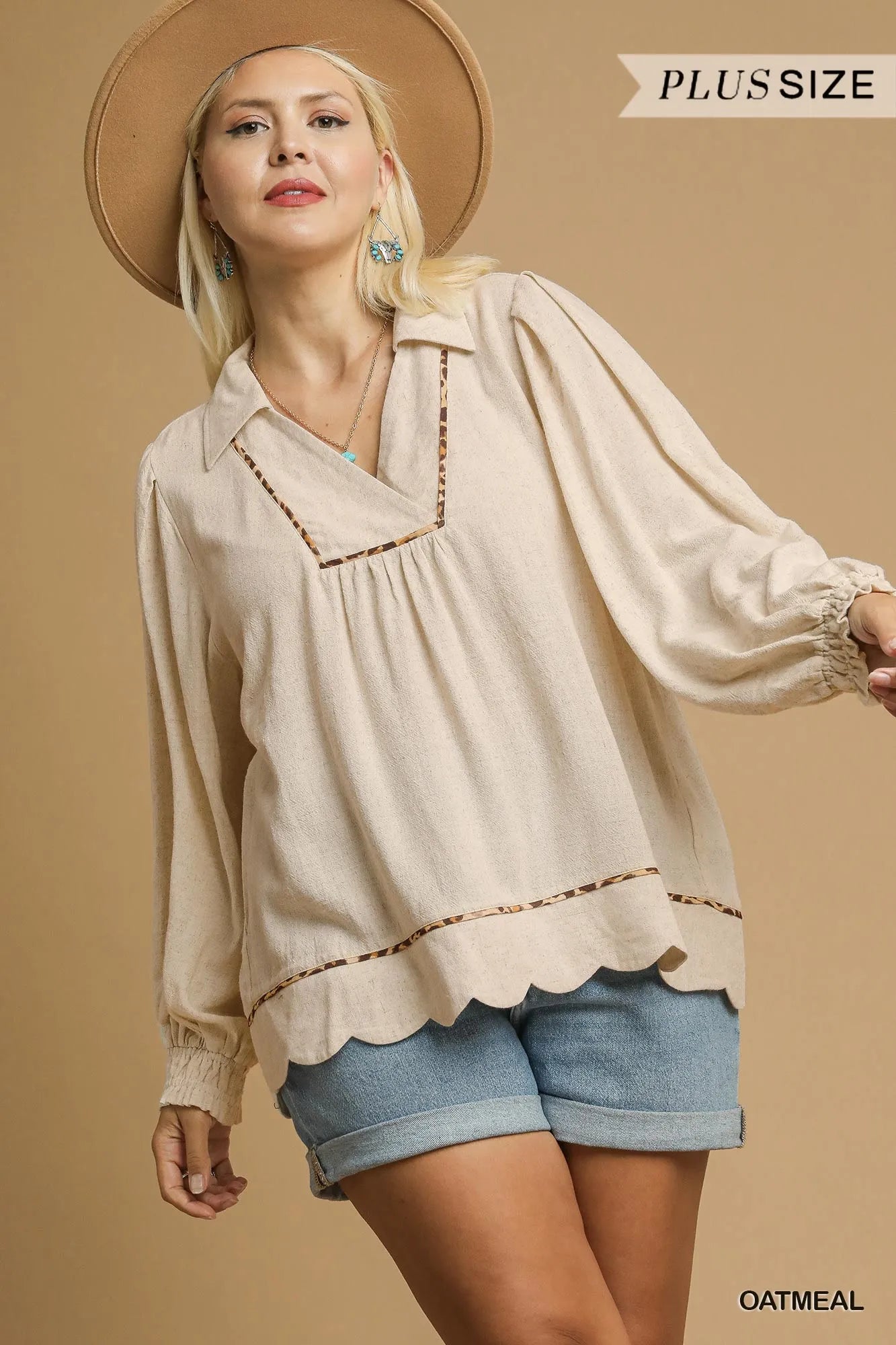 Plus-size oatmeal linen blouse with scallop hem and contrast trim, modeled with wide-brim hat and denim shorts.