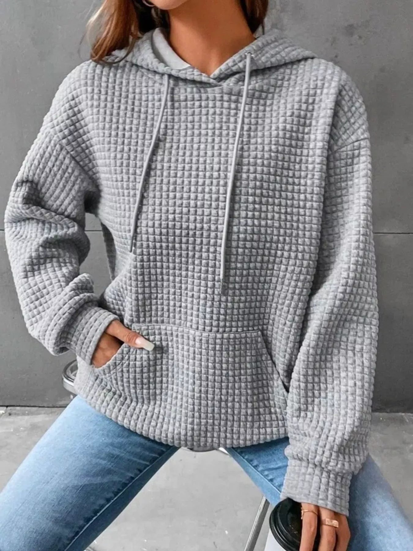 Gray waffle knit hoodie with drawstring hood and front pocket, modeled on a woman.