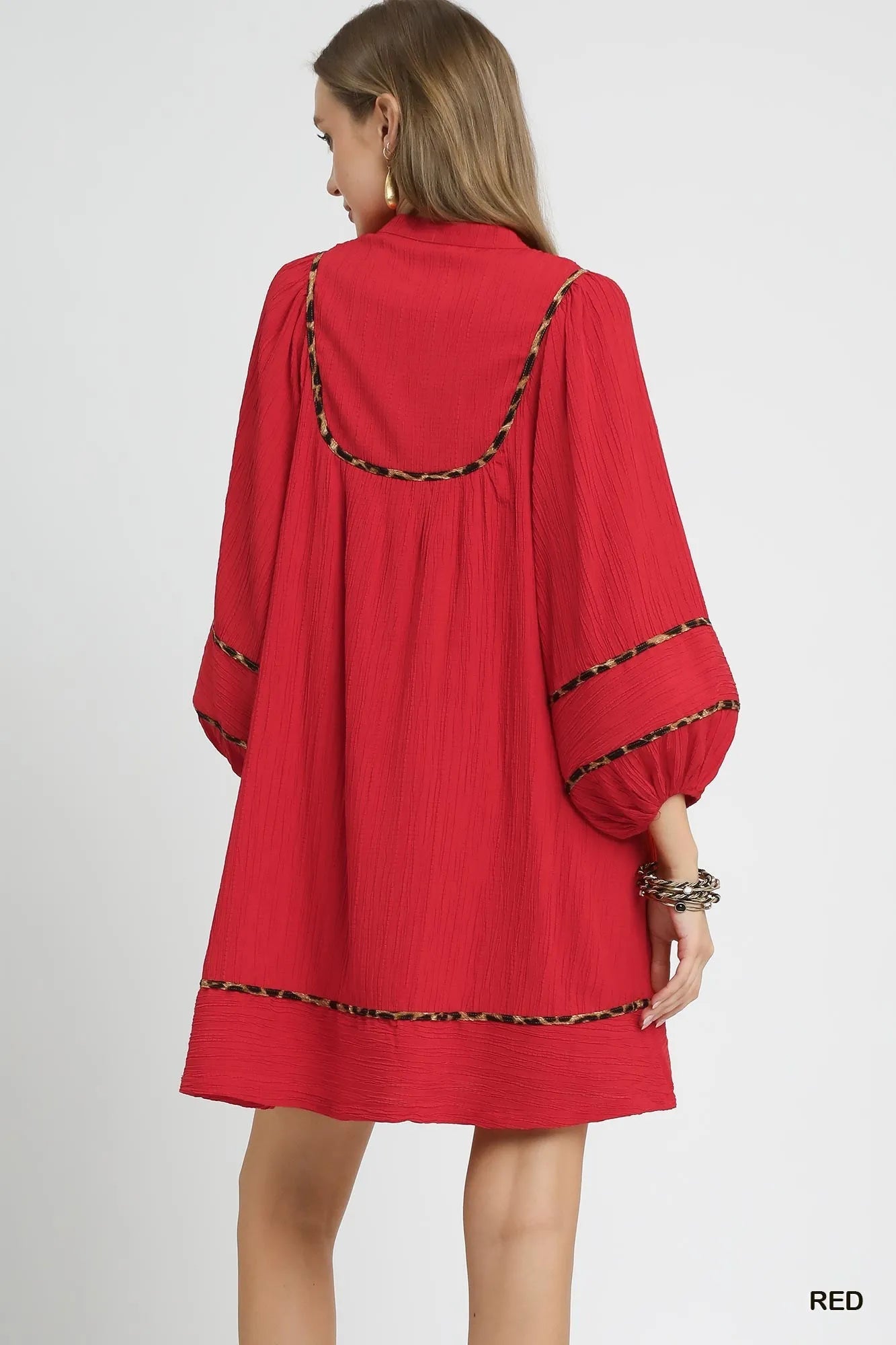 Rear view of red textured babydoll dress with leopard trim and puffed sleeves.