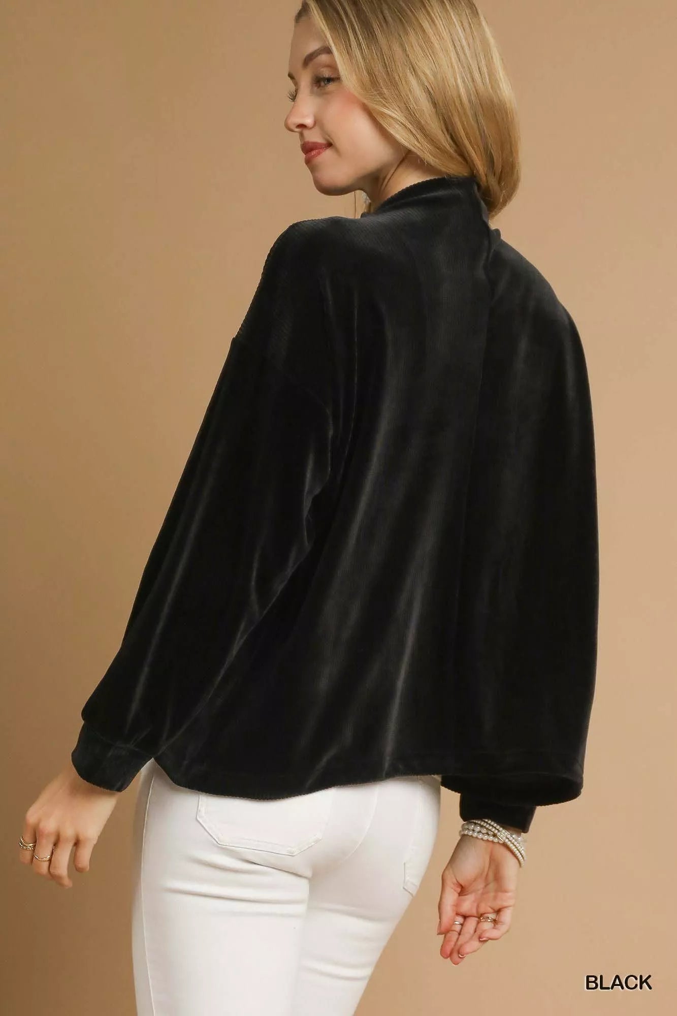 Rear view of black ribbed drawstring hem knit top on model with white pants.