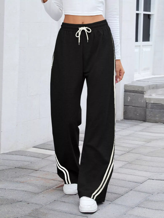 Black side striped wide leg pants with drawstring waist, modeled on a woman outdoors.